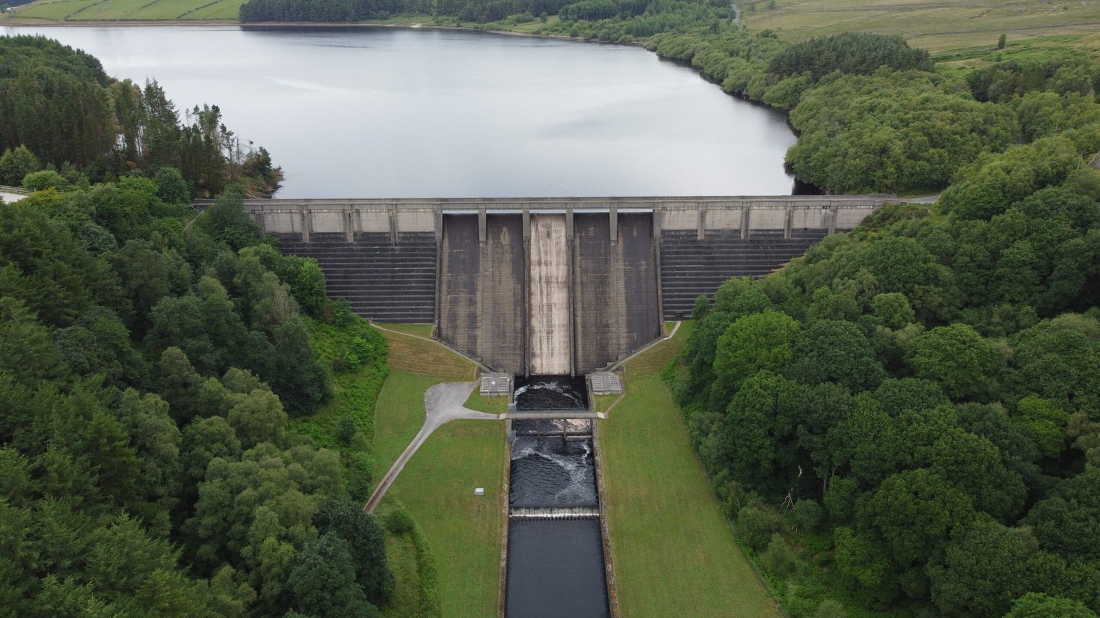 A large concrete dam holding back a reservoir surrounded by green hills and trees in Yorkshire.